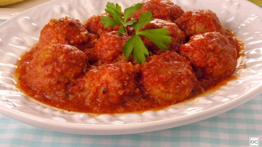 Foto mostra almôndegas com molho em um prato branco em cima da mesa.