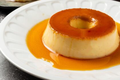 Imagem de um pudim pequeno em um prato branco com bordas ornamentadas