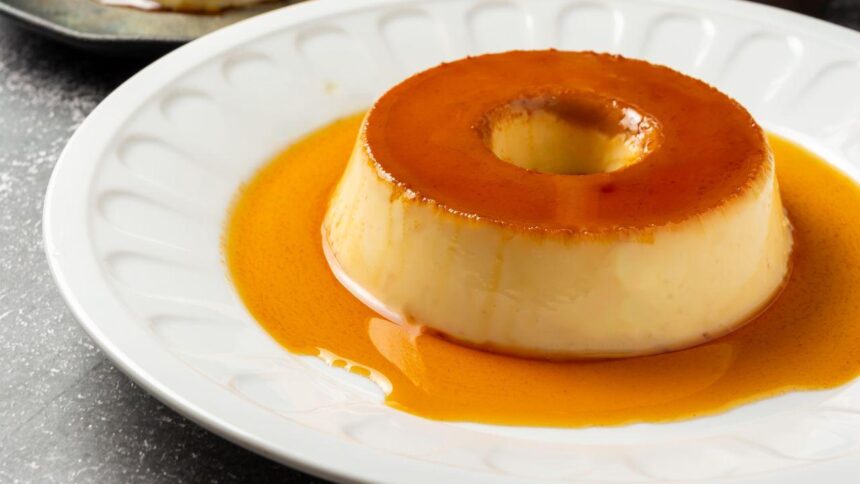 Imagem de um pudim pequeno em um prato branco com bordas ornamentadas