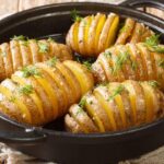 Foto mostra batatas hasselback dentro de uma panela em cima da mesa.