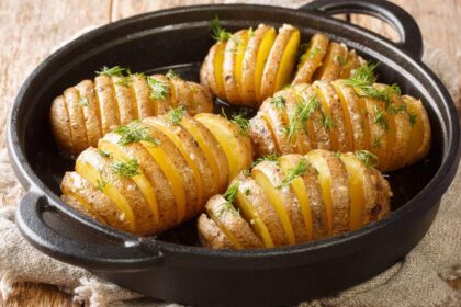 Foto mostra batatas hasselback dentro de uma panela em cima da mesa.