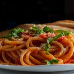 Foto mostra um prato de macarronada com molho vermelho dentro de um prato em cima da mesa.