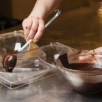 Foto mostra mulher colocando chocolate derretido em formas de ovos de Páscoa.