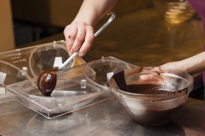 Foto mostra mulher colocando chocolate derretido em formas de ovos de Páscoa.