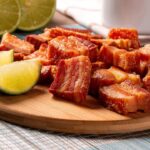 Imagem de pedaços de torresmo em uma tábua de madeira com rodelas de limão ao lado