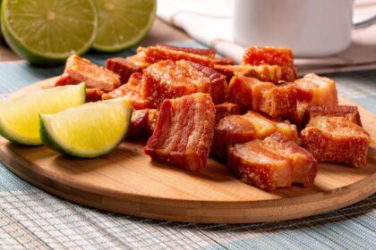 Imagem de pedaços de torresmo em uma tábua de madeira com rodelas de limão ao lado