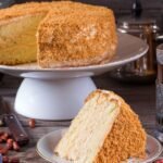 Imagem de um bolo em uma boleira alta e uma fatia em um prato