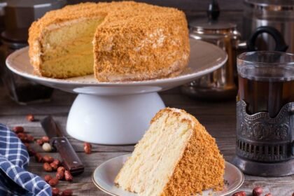 Imagem de um bolo em uma boleira alta e uma fatia em um prato