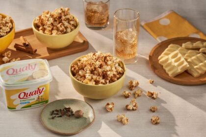 Imagem de pipocas em potes de cerâmicas em uma mesa, acompanhadas de copos de refrigerante com gelo e um pote grande de margarina Qualy