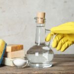 Imagem de um vidro de vinagre ao lado de esponjas de cozinha e uma mão com luva amarela