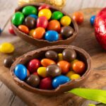 Foto mostra um ovo de Páscoa de chocolate em cima de uma mesa de madeira recheado com confete.