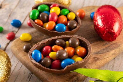 Foto mostra um ovo de Páscoa de chocolate em cima de uma mesa de madeira recheado com confete.