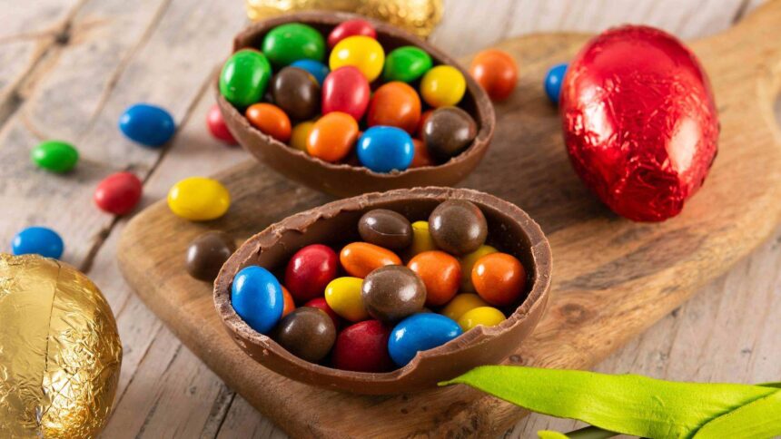 Foto mostra um ovo de Páscoa de chocolate em cima de uma mesa de madeira recheado com confete.
