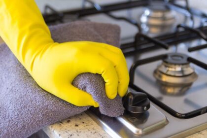 Imagem de uma pessoa de luva amarela limpando o fogão