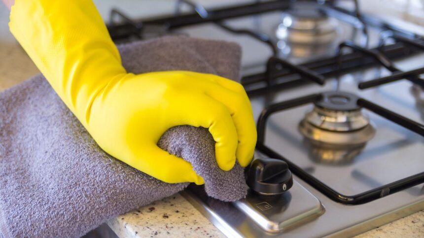Imagem de uma pessoa de luva amarela limpando o fogão