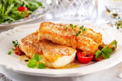 Imagem de dois pedaços de tilápia assada com molho em um prato branco