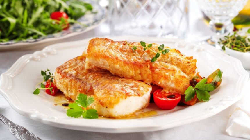 Imagem de dois pedaços de tilápia assada com molho em um prato branco