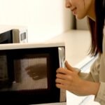 Foto mostra mulher abrindo o micro-ondas em cima da bancada.
