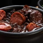 Foto mostra uma panela de ferro de feijoada quente em cima de uma mesa.