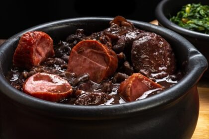 Foto mostra uma panela de ferro de feijoada quente em cima de uma mesa.