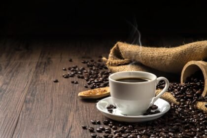 Foto mostra uma xícara de café em cima da mesa com grãos de café ao lado.