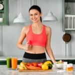 Mulher na frente da bancada cheia de frutas na cozinha.