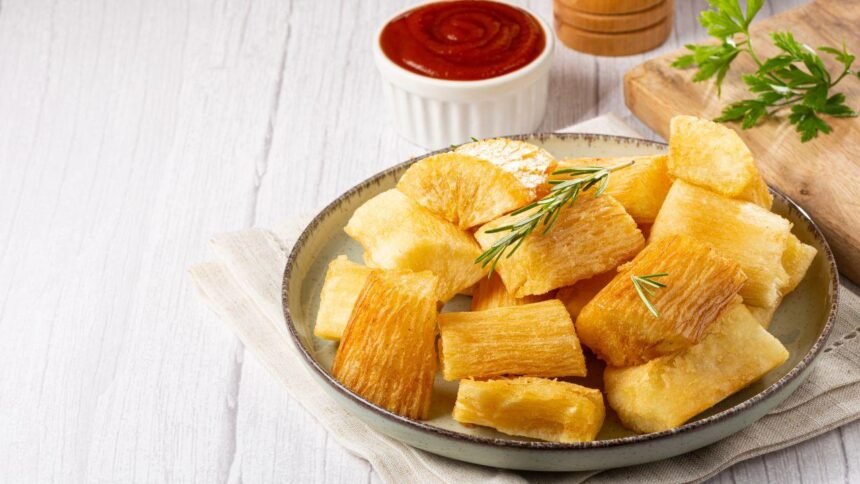 Imagem de uma porção de mandioca frita em um prato com molho vermelho ao fundo