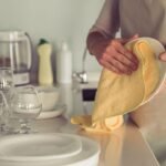 Imagem de uma pessoa secando louças com um pano de prato amarelo claro