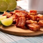 Foto mostra torresmo frito em cima de uma tábua com um limão ao lado.