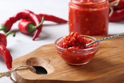 Imagem de um molho de pimenta em um pequeno pote de vidro com pimentas dedo de moça ao redor