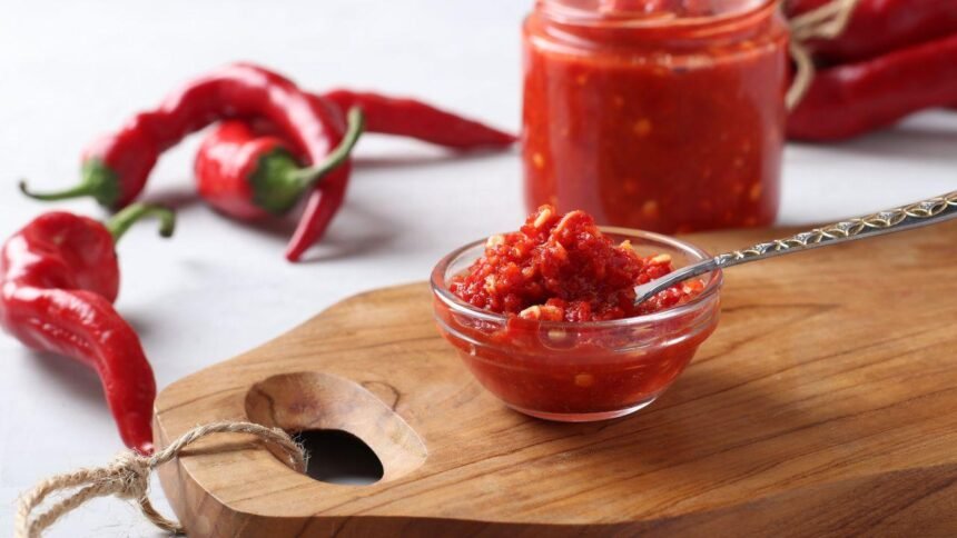 Imagem de um molho de pimenta em um pequeno pote de vidro com pimentas dedo de moça ao redor