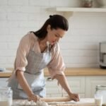 Mulher branca, cabelo castanho, cozinhando na cozinha.