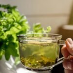 Foto mostra uma xícara de chá verde com folhas de hortelã ao lado.