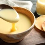 Imagem de uma colher levantando leite condensado que está em um pote