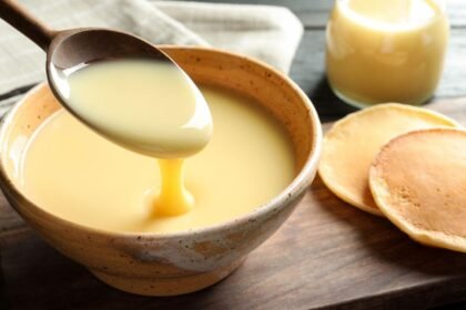 Imagem de uma colher levantando leite condensado que está em um pote