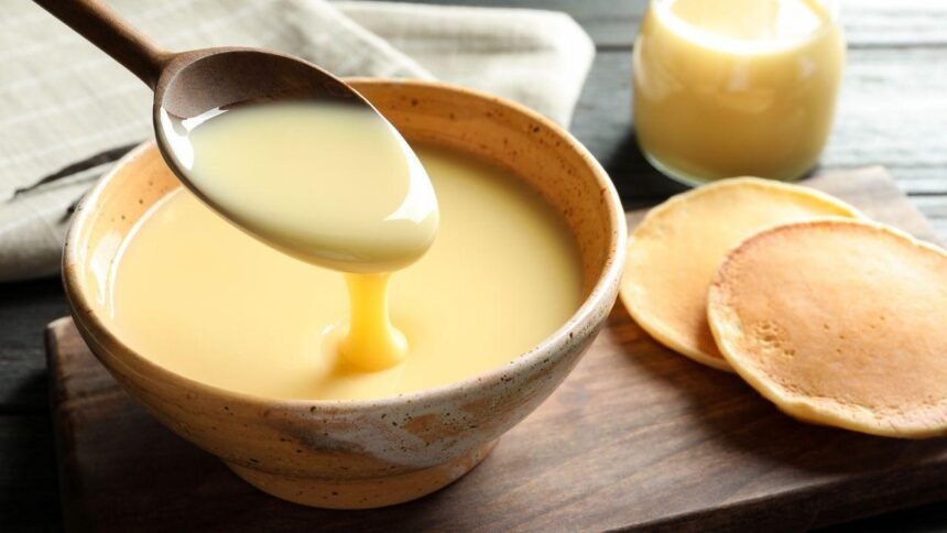 Imagem de uma colher levantando leite condensado que está em um pote