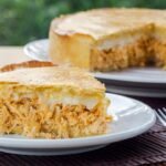 Imagem de uma fatia de torta de frango com requeijão com o restante da torta atrás