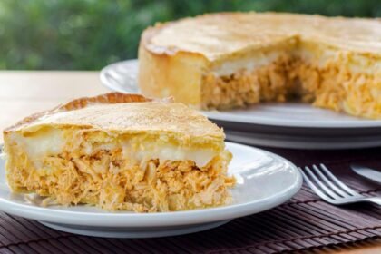 Imagem de uma fatia de torta de frango com requeijão com o restante da torta atrás