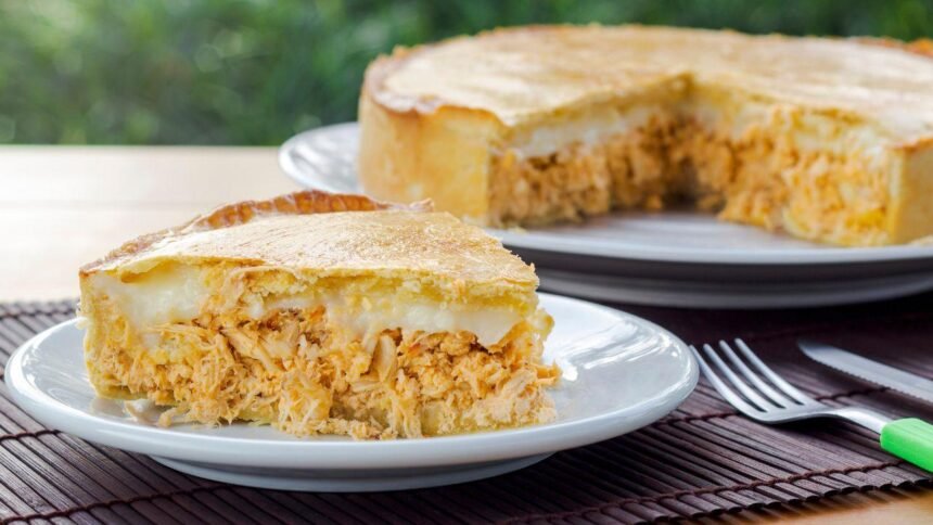Imagem de uma fatia de torta de frango com requeijão com o restante da torta atrás