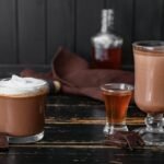 Foto mostra chocolates quentes dentro de caneca em cima da mesa.