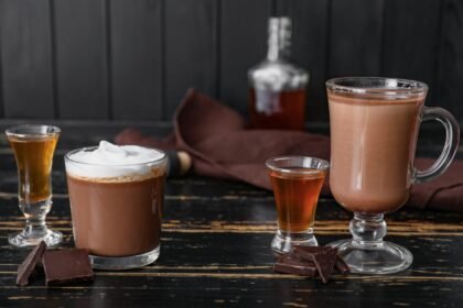 Foto mostra chocolates quentes dentro de caneca em cima da mesa.