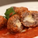Foto mostra almôndegas de carne recheada com queijo com molho dentro de um prato.