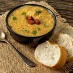 Foto mostra um prato fundo com caldo de frango, ao lado tem torradas de pão.