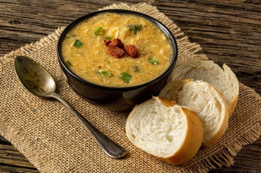 Foto mostra um prato fundo com caldo de frango, ao lado tem torradas de pão.