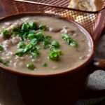 Foto mostra uma panela de porcelana com caldo de feijão em cima de uma tábua.
