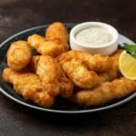 Prato com pedaços de peixe frito do lado de um molho e limão cortado.