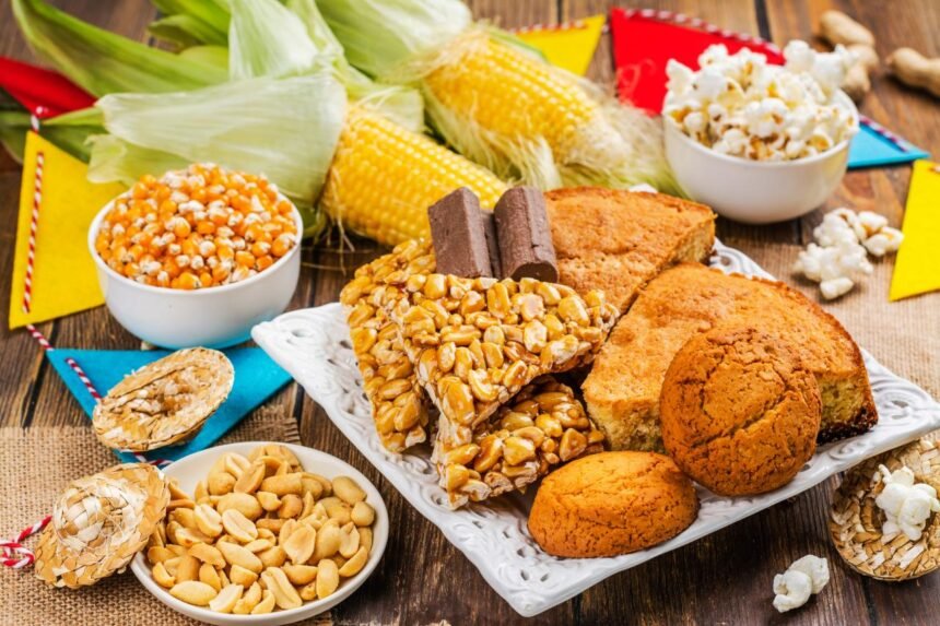 Foto mostra milho, paçoca, amendoim, broa de milho em cima de uma mesa.