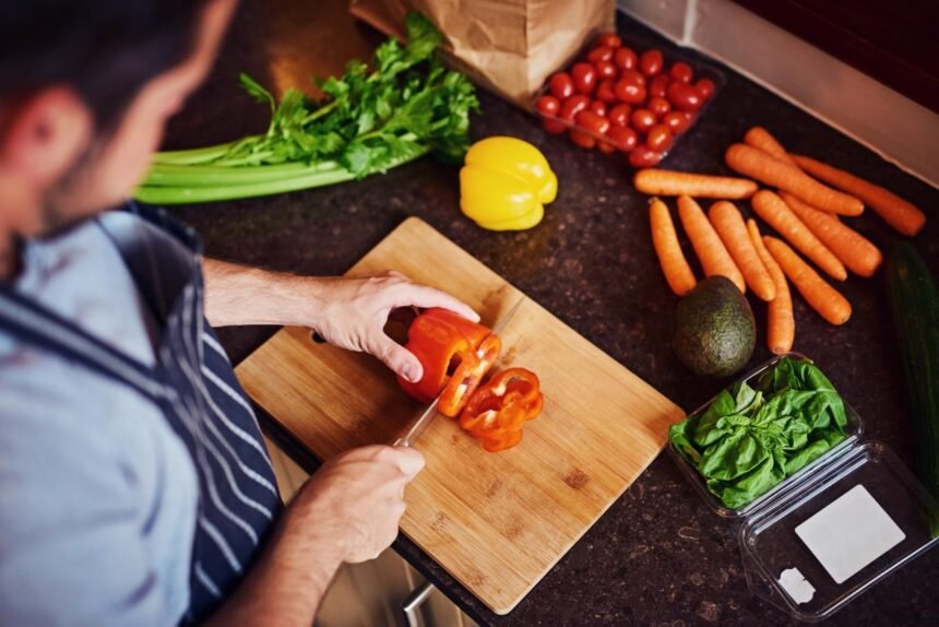 Foto mostra pessoa cortando legumes em uma tábua na bancada da cozinha.