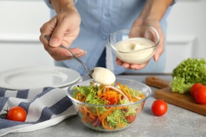 Foto mostra uma pessoa colocando molho na salada em um pote de vidro.