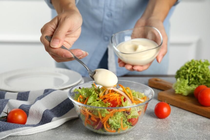 Foto mostra uma pessoa colocando molho na salada em um pote de vidro.